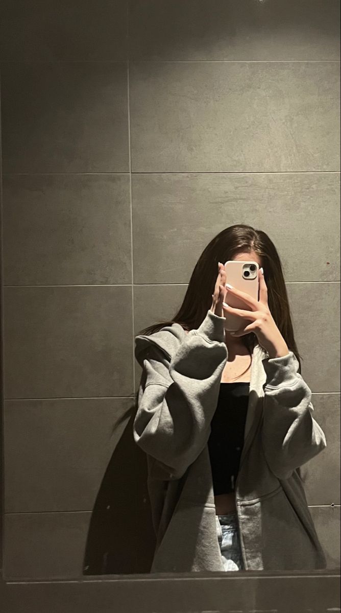 a woman taking a selfie with her cell phone in front of a wall mounted mirror