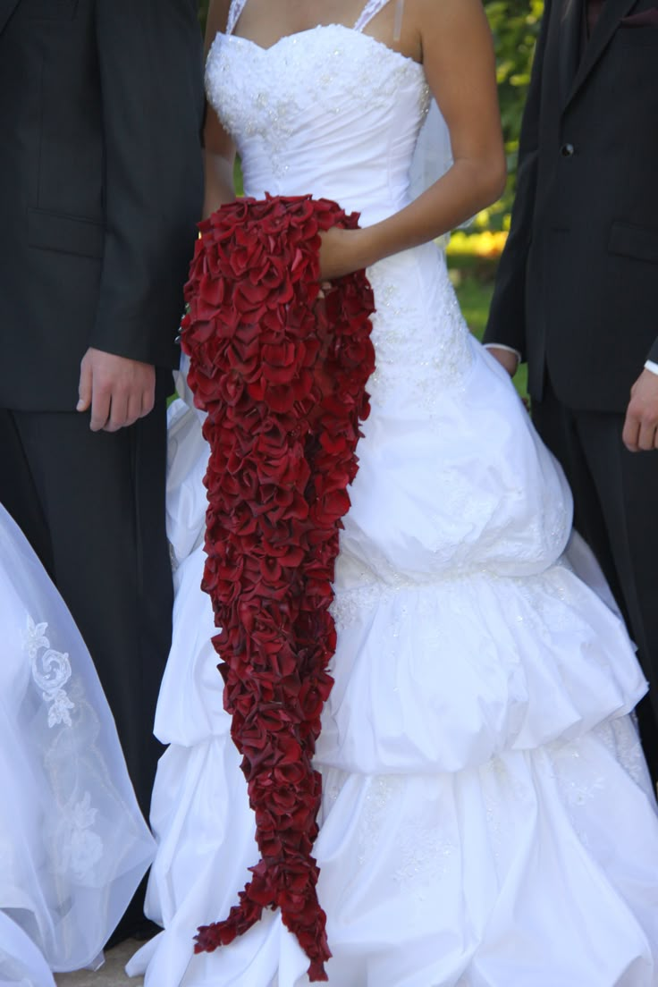 a woman in a wedding dress holding a red flowered shawl while standing next to two men