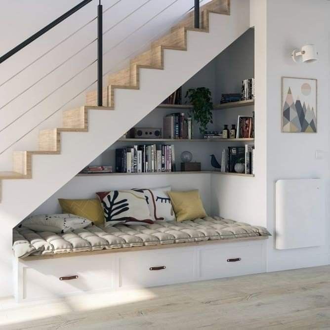 there is a bench under the stairs in this room with bookshelves and pillows