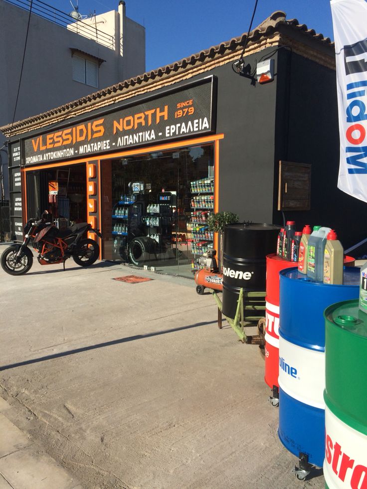 a motorcycle shop on the street in front of a building with several different colored barrels