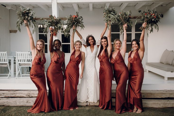 a group of women standing next to each other in front of a house holding flowers