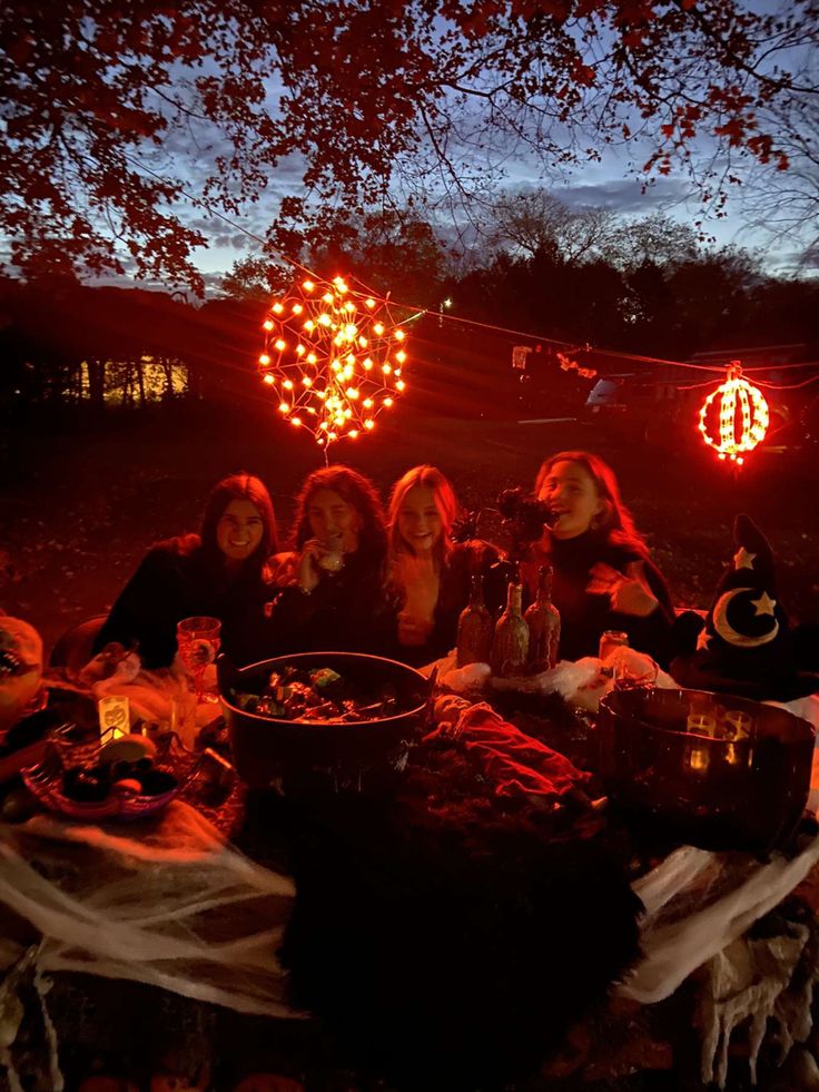 a group of women sitting around a table with food and drinks on it at night