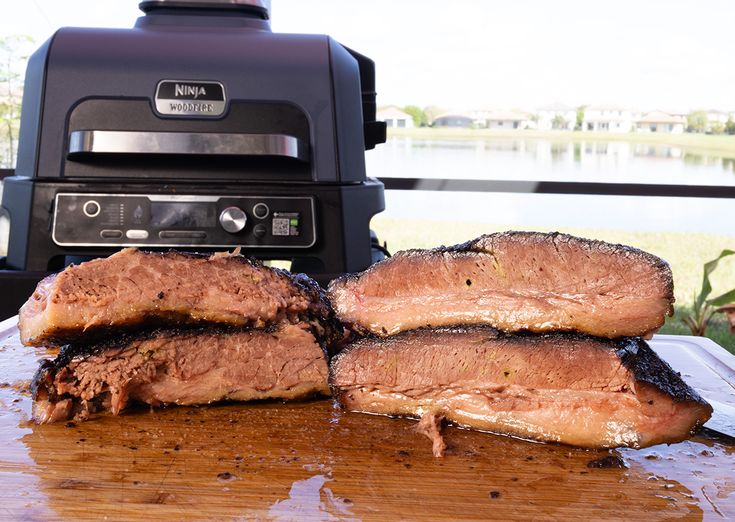 three pieces of meat sitting on top of a cutting board next to an open grill