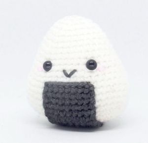 a small crocheted stuffed animal with black eyes and a white face, sitting on a white surface