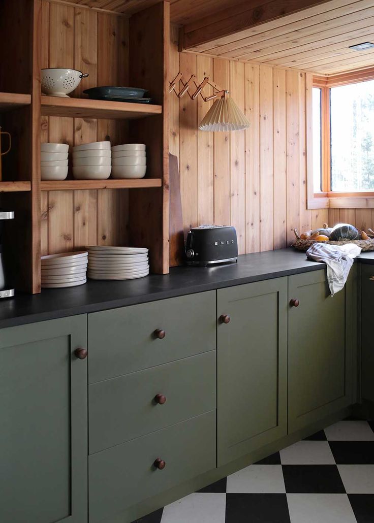 a kitchen with black and white checkered flooring, green cabinets and open shelving