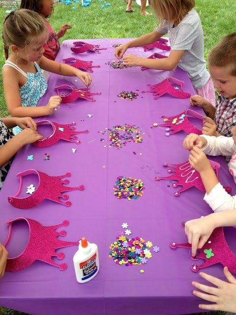 several children are sitting at a purple table with pink decorations on it and one child is reaching for something