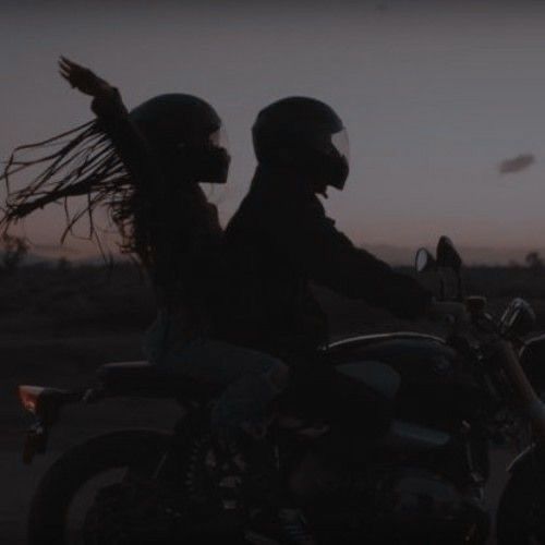 two people riding on the back of a motorcycle at sunset with long hair blowing in the wind