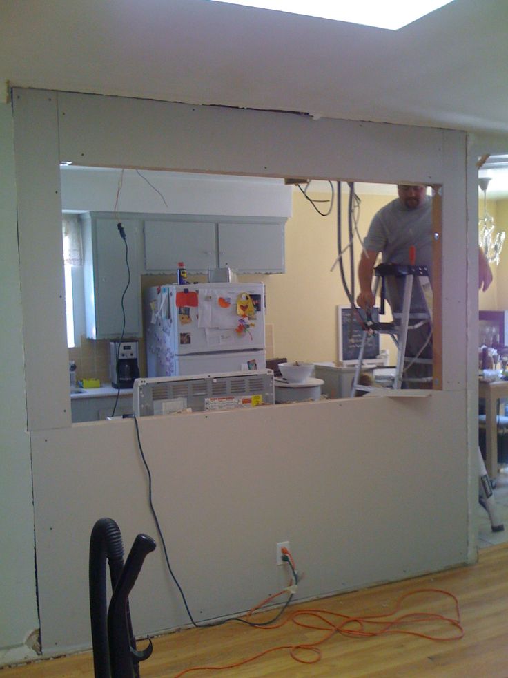 a man is working on the wall in his kitchen while another person stands behind him