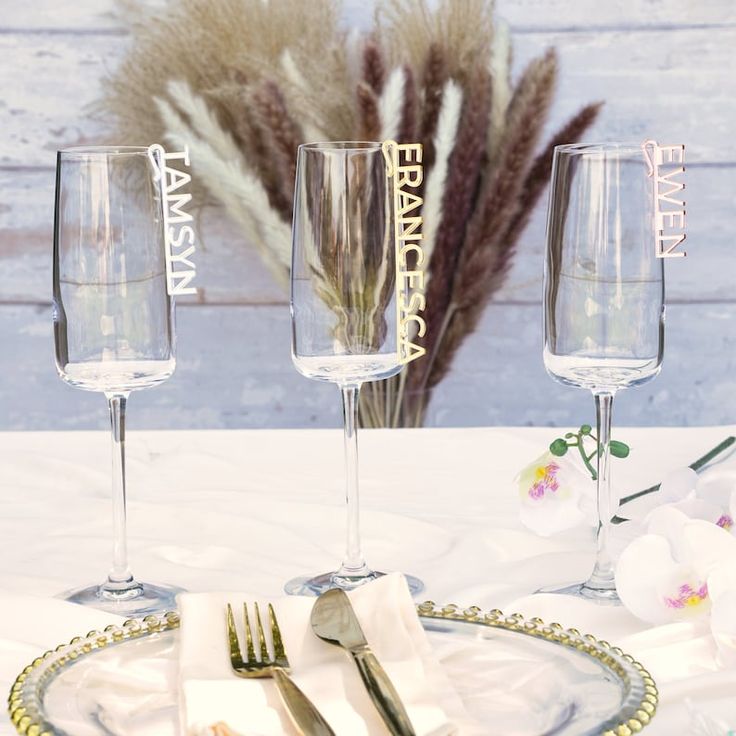 three empty wine glasses sitting on top of a table next to silverware and flowers