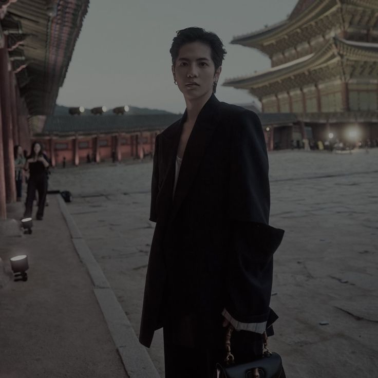 a man standing in front of a building holding a handbag and looking at the camera