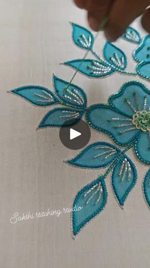 someone is working on something that looks like blue flowers with green leaves and beading