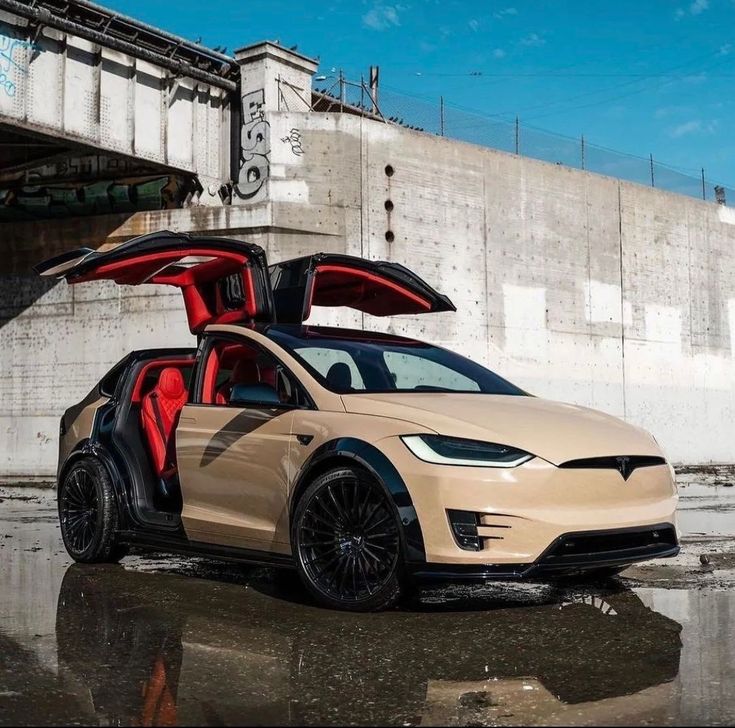 an electric car with its doors open sitting in front of a concrete wall under a bridge