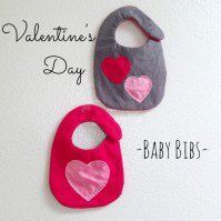 two baby bibs with hearts on them hanging from the wall next to each other