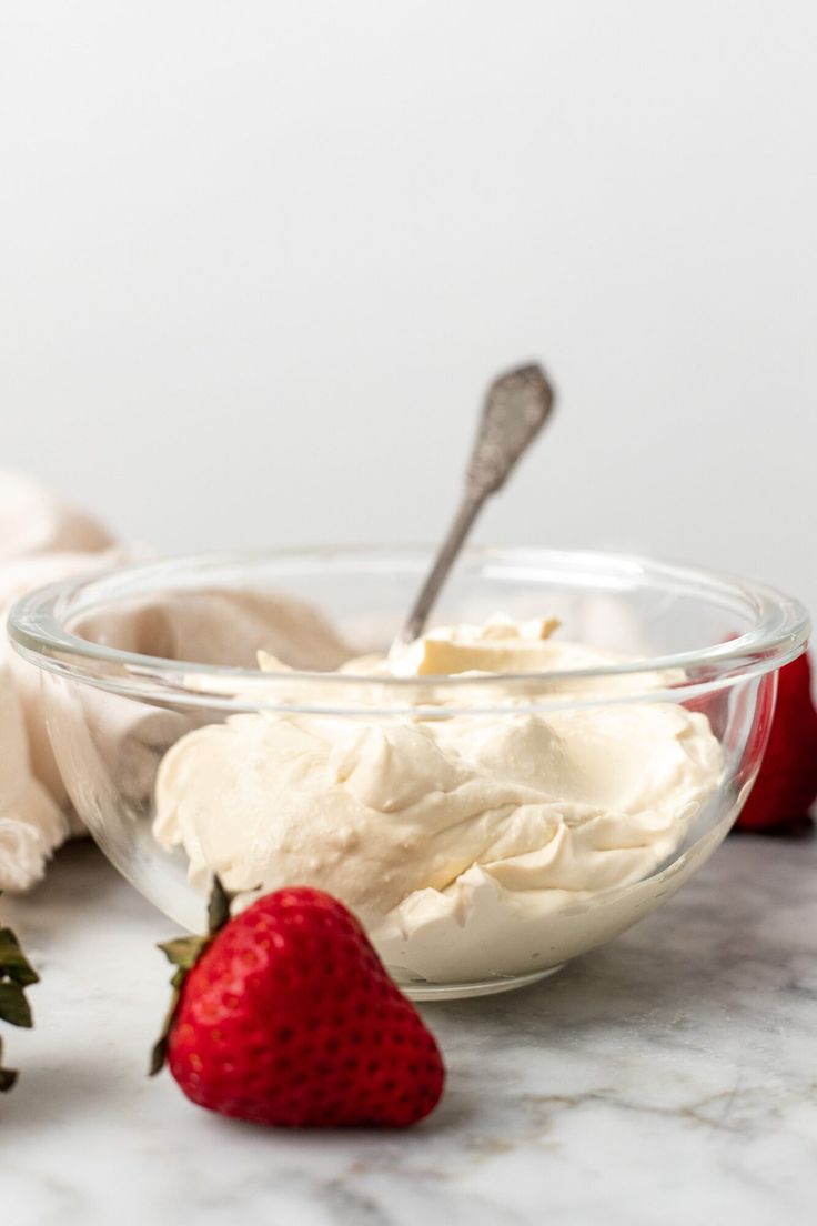 strawberries and whipped cream in a glass bowl on a marble counter with two forks