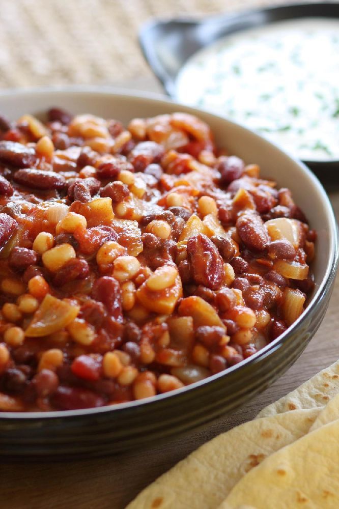 a bowl filled with beans and corn next to tortillas