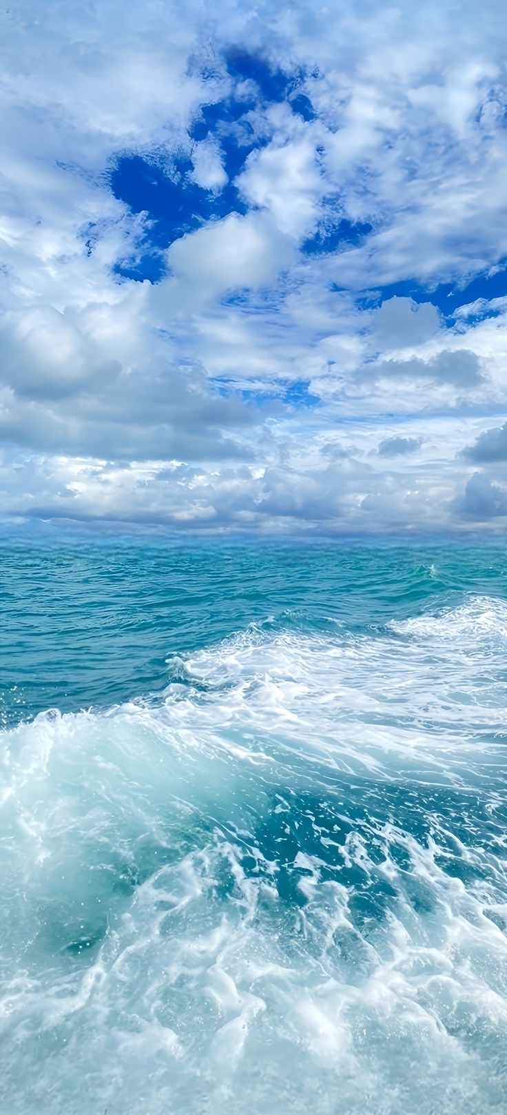 the ocean is blue and green with white clouds in the sky above it, as well as waves on the water