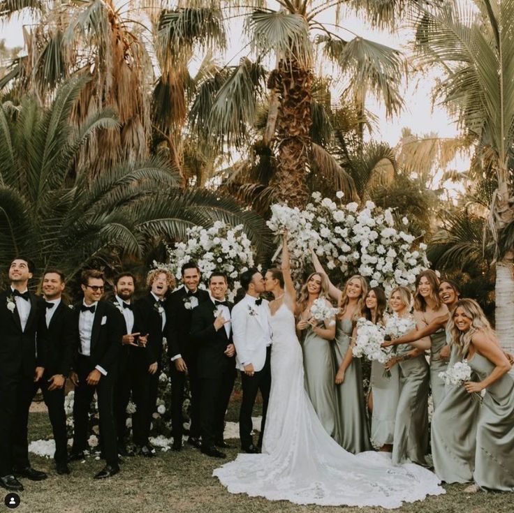 a group of people standing next to each other in front of palm trees and flowers