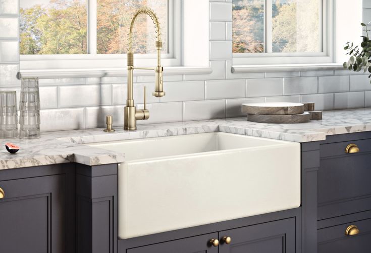 a white kitchen sink sitting under a window next to a counter top with gold faucets