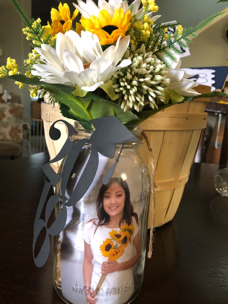 there is a vase with flowers in it and a photo on the bottom, sitting on a table