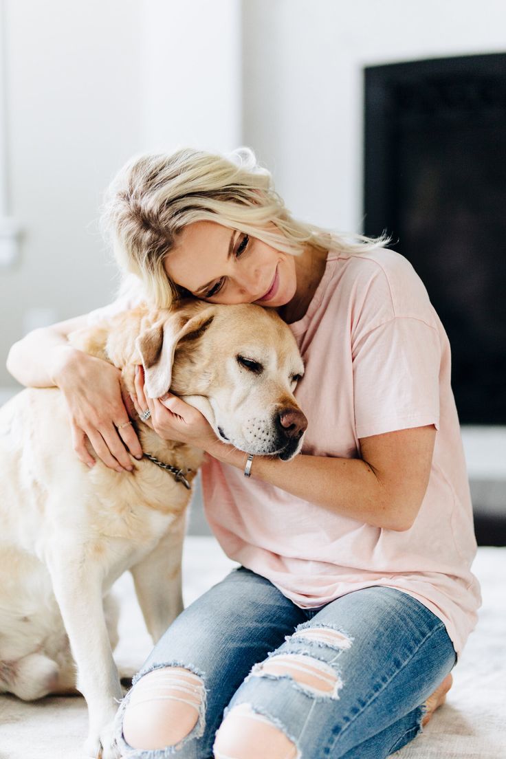 a woman is sitting on the floor hugging her dog's face while she holds it up