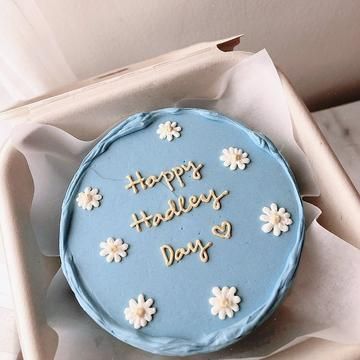 a blue cake with white flowers on it sitting in a box that says happy holidays and days