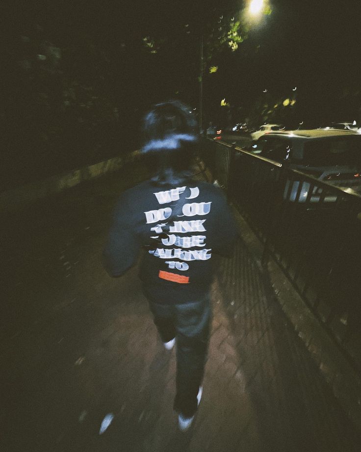 a man walking down a sidewalk at night with his back turned to the camera,