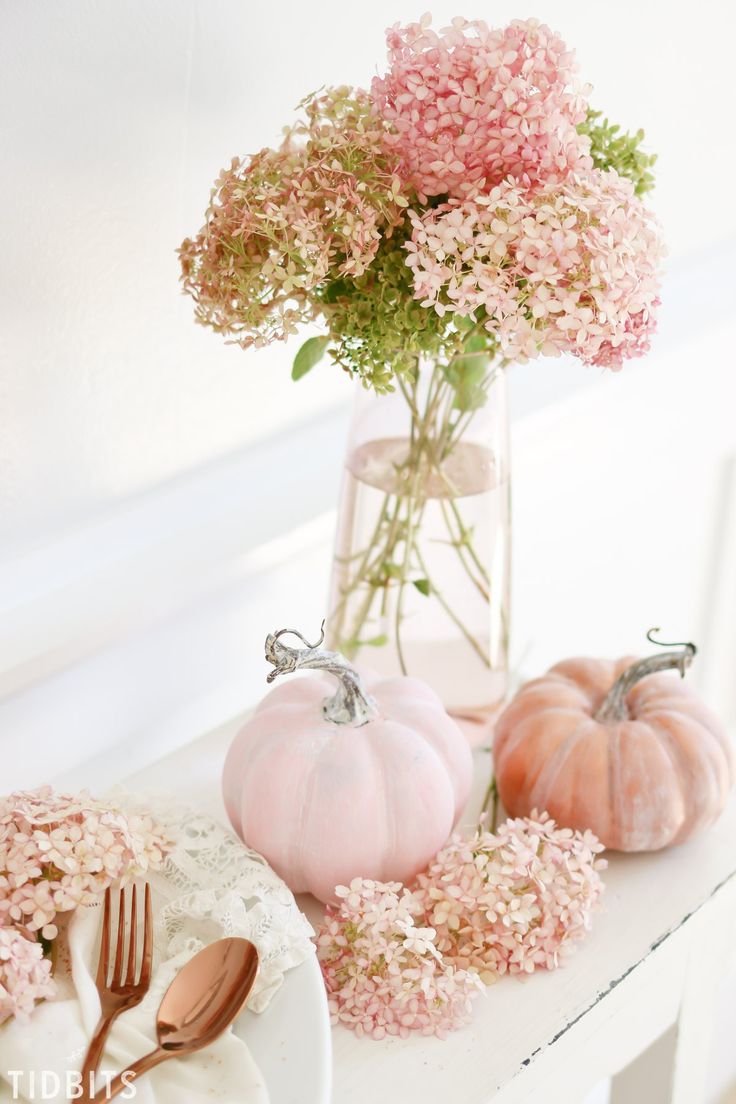 pink flowers in a glass vase on a white table with plates and utensils