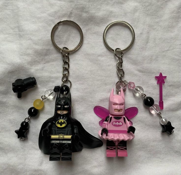 two lego keychains with batman and batgirl on them, one is pink the other is black