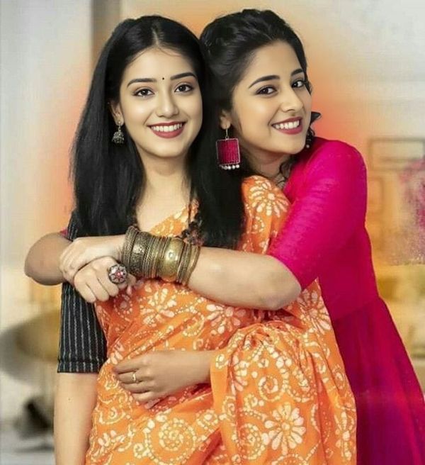 two women are hugging each other in an orange and pink sari with gold accents