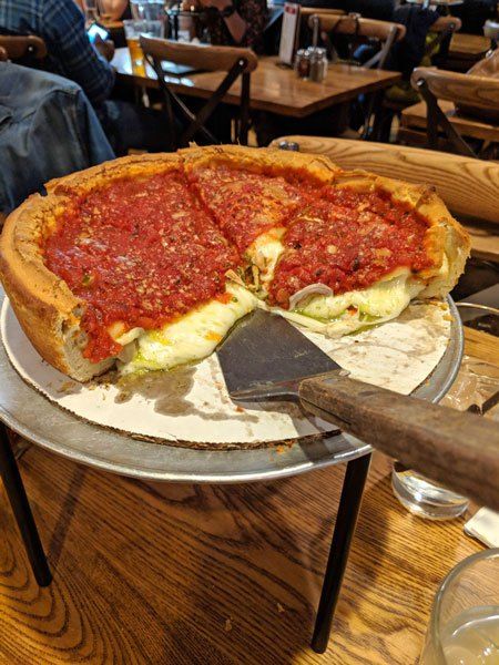 a deep dish pizza on a metal platter with one slice taken out and people sitting at tables in the background