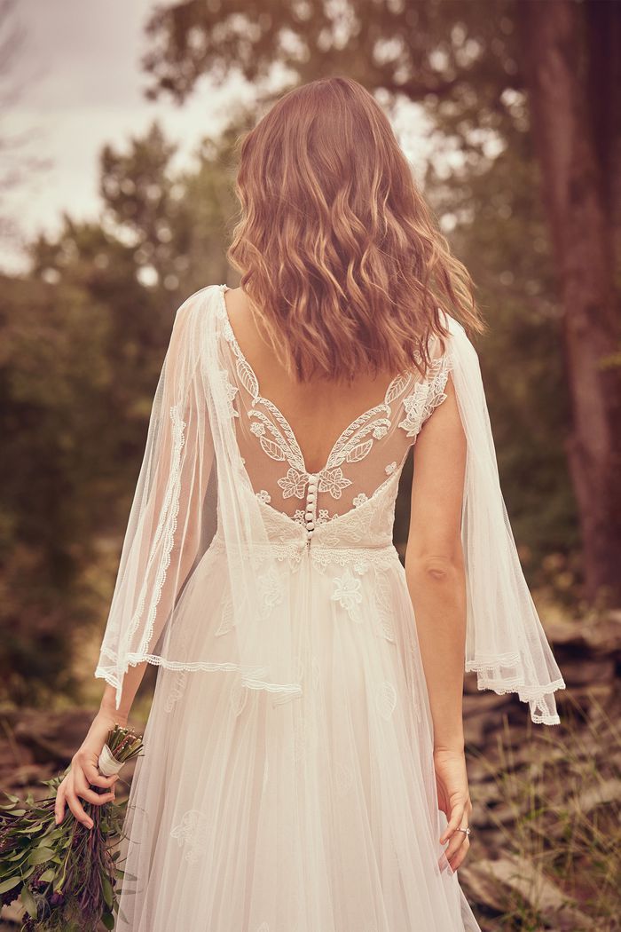 a woman in a wedding dress is walking through the woods with her back to the camera