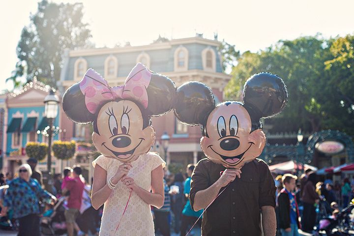 two people in mickey and minnie mouse ears walking down the street with balloons on their heads