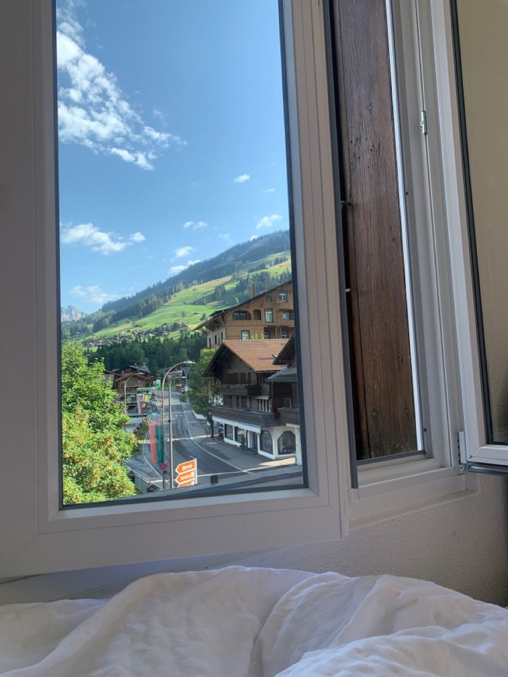 a window view of a town and mountains from inside a bedroom with a white comforter on the bed