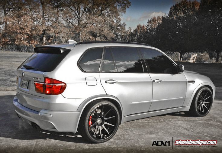 the rear end of a white bmw suv parked in a parking lot with trees behind it