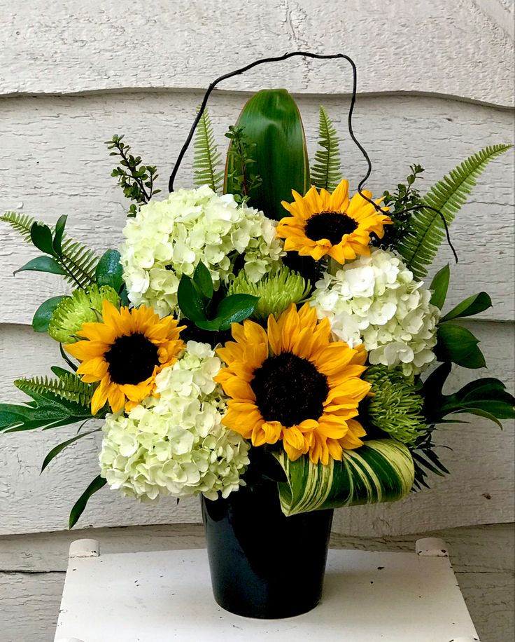 a black vase filled with white and yellow flowers