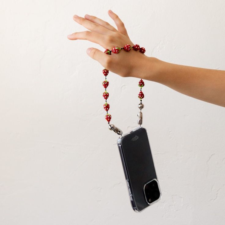 a hand holding a cell phone with beads on it's wrist and a chain attached to it