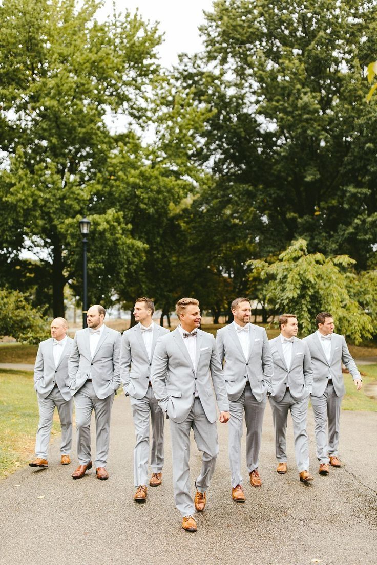 a group of men in grey suits walking down a street next to trees and grass