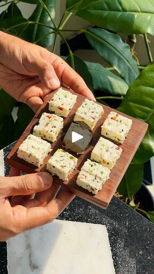 someone is holding up some food on a wooden board in front of green plants and potted plants