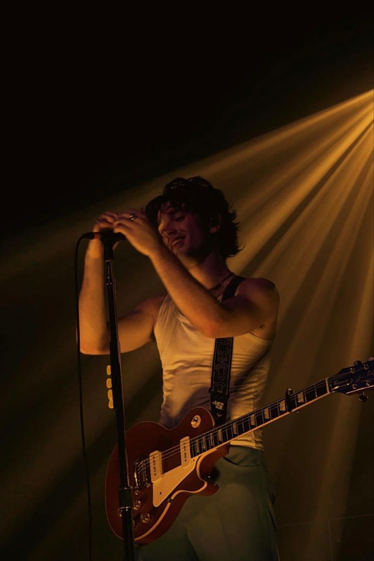 a man standing in front of a microphone holding a guitar