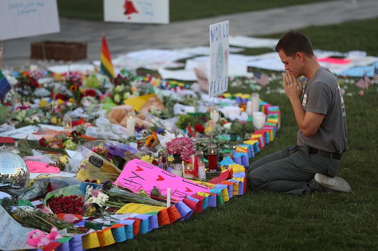 a man sitting on the ground in front of flowers and candles at a makeshift memorial