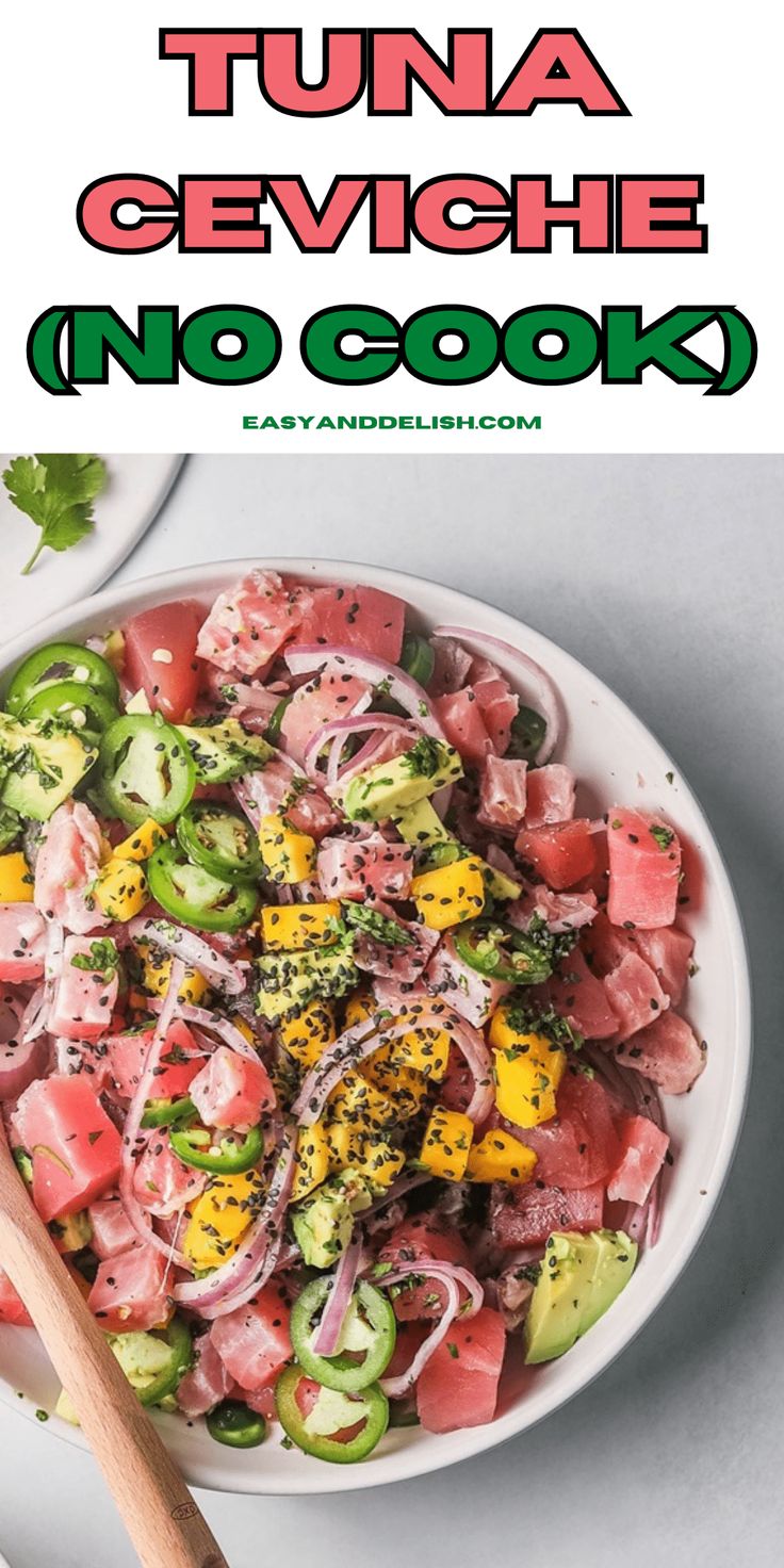 a white bowl filled with tuna and veggies on top of a table next to a wooden spoon