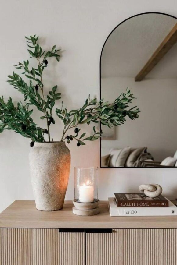 a vase filled with greenery sitting on top of a wooden dresser next to a mirror