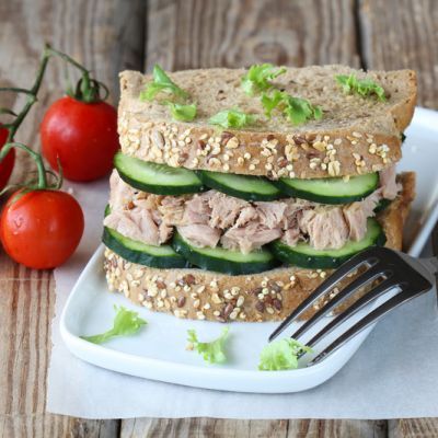 sandwich with tuna, cucumber and lettuce on white plate next to tomatoes