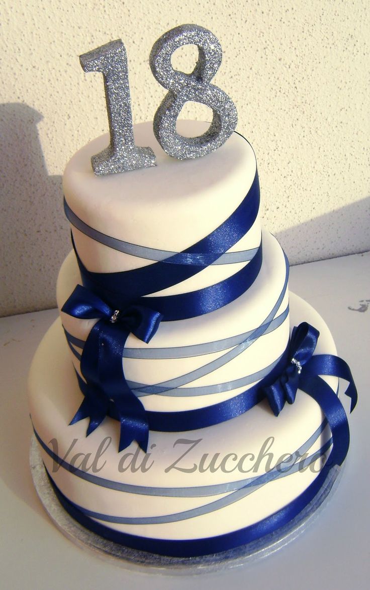 a three tiered white cake with blue ribbon and silver numbers on the bottom layer