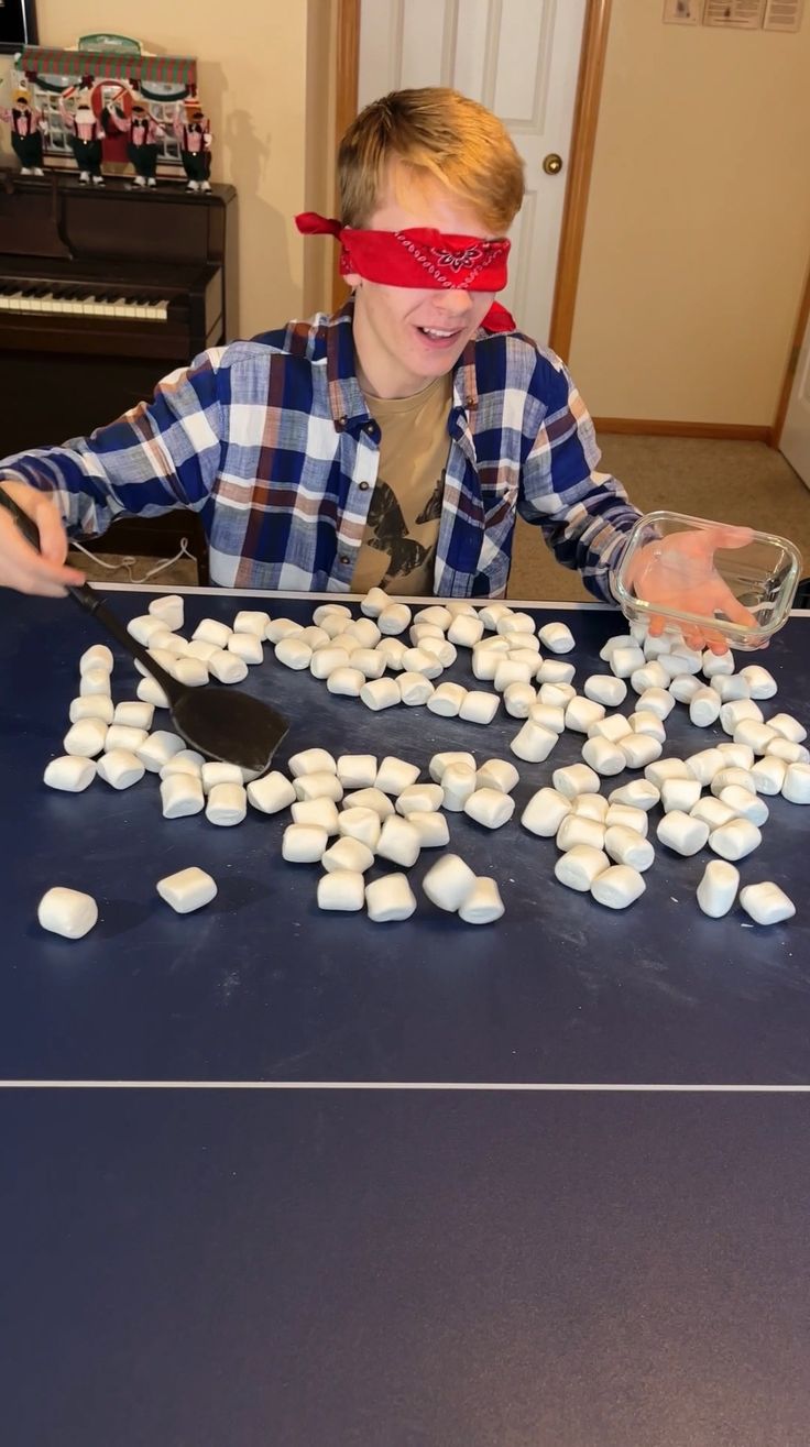 a young boy wearing blindfolds and making marshmallows on a table