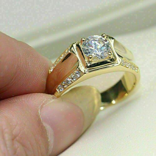 a man's hand holding a yellow gold ring with a diamond in the center