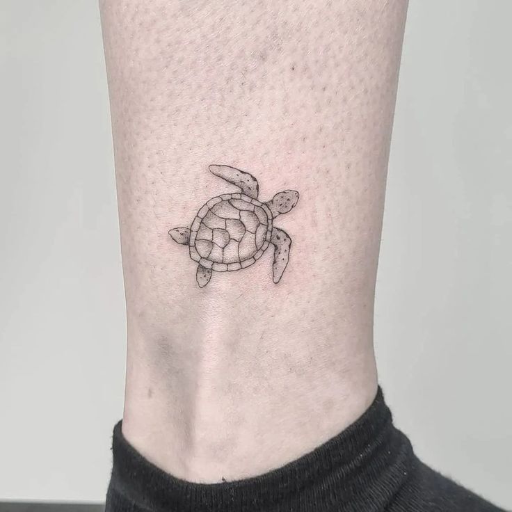 a small turtle tattoo on the side of the ankle is shown in black and white