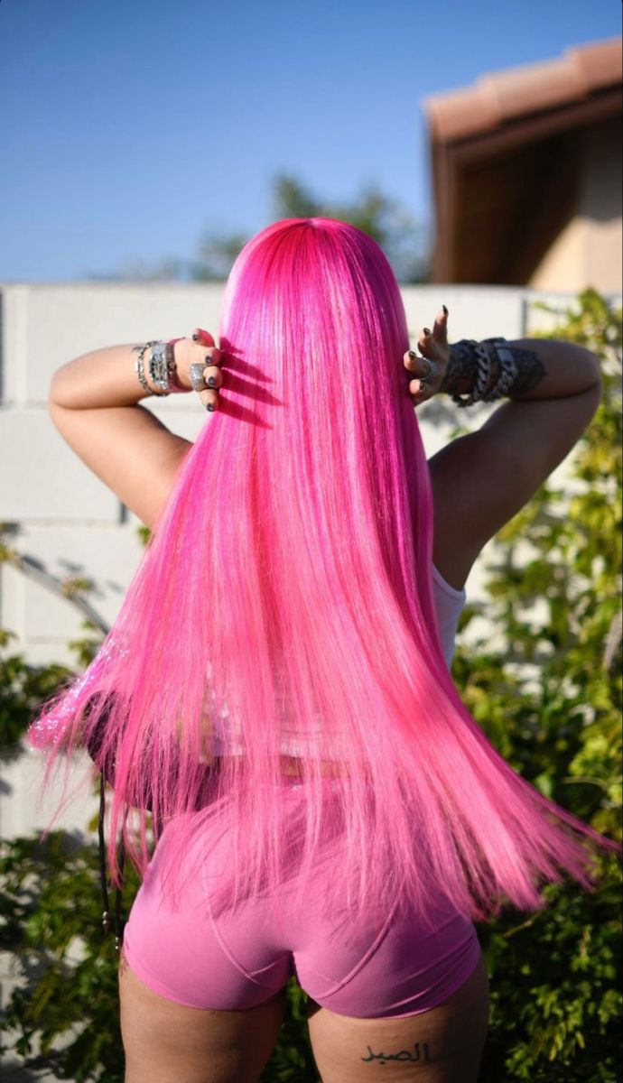 a woman with pink hair and piercings on her head is standing in front of some bushes