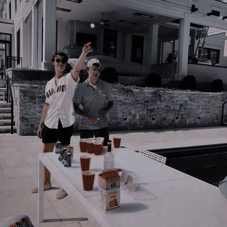 two people standing at a table with cups on it and one person throwing a frisbee in the air