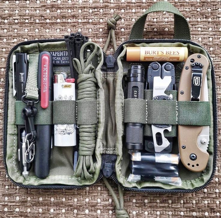 the contents of an outdoor survival kit are neatly packed in a pouch on a woven surface